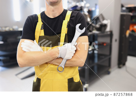 Strong man in yellow overalls holding a wrench Strong man in yellow overalls holding a wrench 87257868