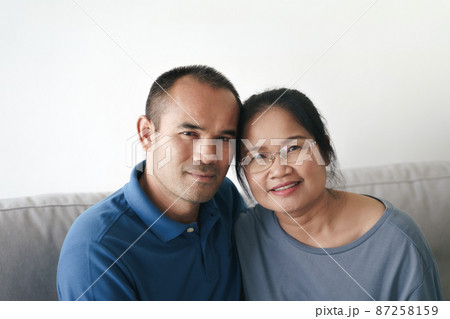 Portrait of Asian mature couple sitting in the living room. wife and husband hugging, holding hand with happiness and cheerful. Love, safety, and insurance family concept. 87258159