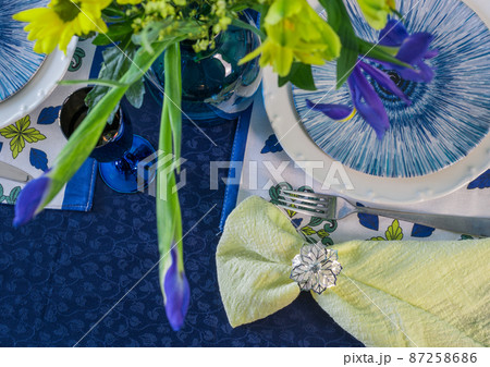 Table setting in blue and yellow colors. On a dark tablecloth a plate, a vase of flowers and decor Table setting in blue and yellow colors. On a dark tablecloth a plate, a vase of flowers and decor 87258686