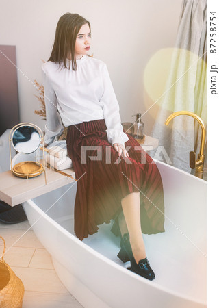 Portrait of fashionable women in red skirt, white blouse and stylish beige high-heeled shoes with a chain buckle posing in a bed 87258754