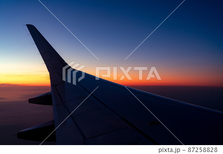 Wing of plane with sunrise skyline. Airplane flying in the sky. Scenic view from airplane window. Commercial airline flight. Plane wing above clouds. International flight. Travel abroad after covid-19 87258828