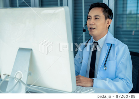 Doctor wearing headset talking actively on video call in a clinic or hospital . 87260789