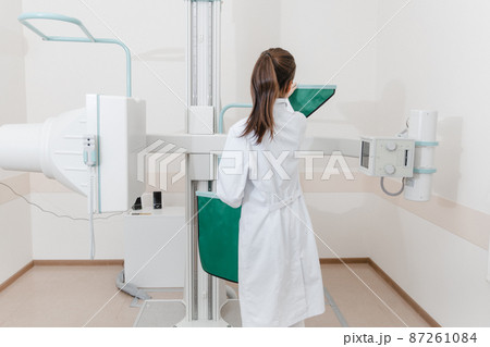 Hospital Radiology Room. Xray machine for fluorography. Doctor radiologist in gown adjusting the X-ray machine for radiography. Medical equipment. Scanning chest, heart or lungs in clinic office. 87261084