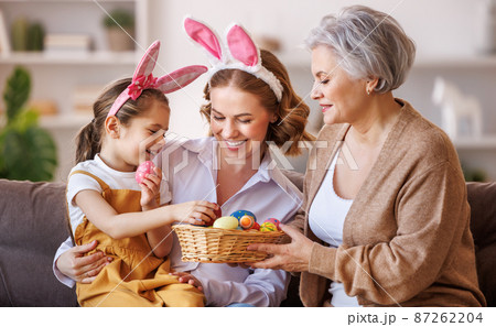 Happy family in bunny ears laugh and play with eggs at home during preparation for Easter holiday Happy family in bunny ears laugh and play with eggs at home during preparation for Easter holiday 87262204