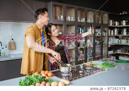 asian couple taking selfie while cooking together in the kitchen 87262378