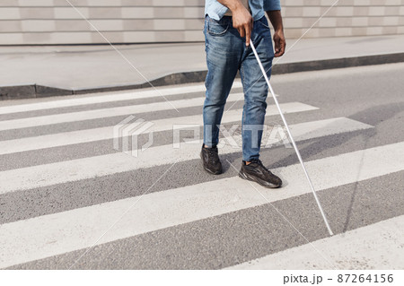 Unrecognizable young black man with vision disability walking across city street, using walking cane outdoors, copy space Unrecognizable young black man with vision disability walking across city street, using walking cane outdoors, copy space 87264156