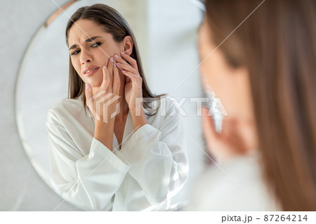 Frustrated Young Woman With Problem Skin Popping Pimple On Cheek Near Mirror Frustrated Young Woman With Problem Skin Popping Pimple On Cheek Near Mirror 87264214