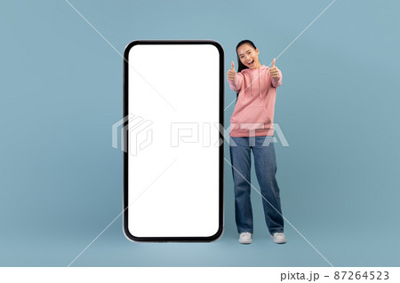 Cheerful asian woman posing with big smartphone, showing thumbs up 87264523