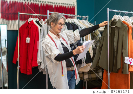 Woman looking at sketch touching hanging blouse 87265171