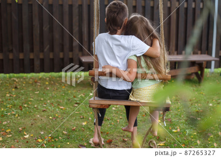 children sitting on a swing in the garden. older brother hugging little sister 87265327