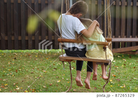 children sitting on a swing in the garden. older brother hugging little sister children sitting on a swing in the garden. older brother hugging little sister 87265329