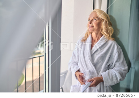 A blonde middle aged woman in a white robe enjoying a sunny day 87265657