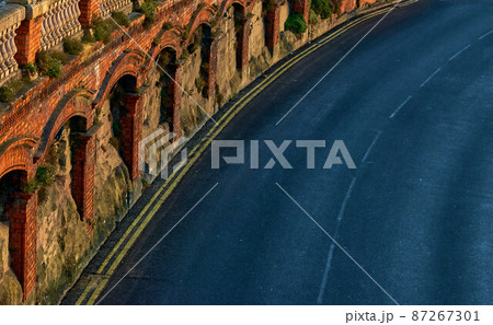 Red brick arches over a black tarmac road 87267301
