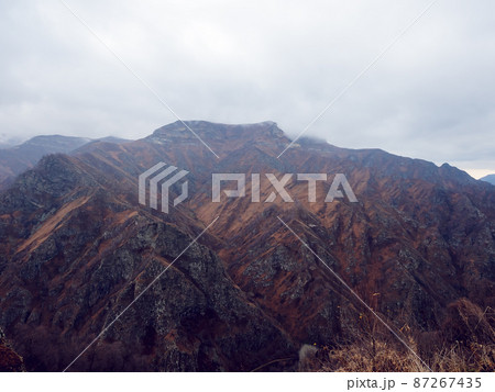 Rocky mountains covered with dry golden grass and bare trees under low hanging clouds. Rocky mountains covered with dry golden grass and bare trees under low hanging clouds. 87267435