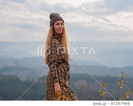 A smiling long-haired lady stands against the backdrop of wooded hills under a cloudy sky. Beauty of the Caucasus. Kislovodsk park 87267469