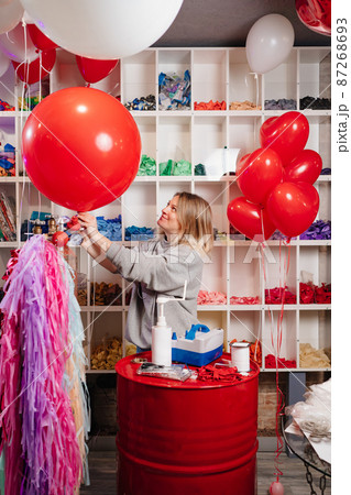 a woman inflates of helium from a big red balloon. 87268693
