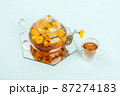 Herbal tea. Transparent glass teapot, cups of tea with orange flowers of calendula on a blue background. Calming drink concept 87274183