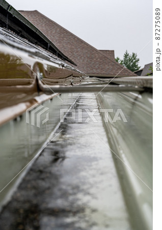 Selective focus on a section of residential guttering with hanger conveying water during a storm. Rain splatters and drops visible. Selective focus on a section of residential guttering with hanger conveying water during a storm. Rain splatters and drops visible. 87275089