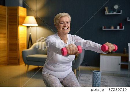 Senior woman training with dumbbells at home 87280719