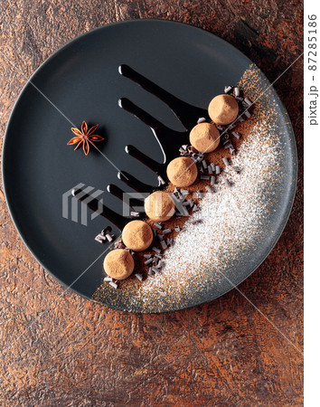 Chocolate truffles on a black plate with chocolate sauce. 87285186