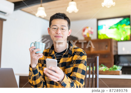 PC作業中にスマートフォンからの連絡で微笑みを浮かべる男性起業家 PC作業中にスマートフォンからの連絡で微笑みを浮かべる男性起業家 87289376