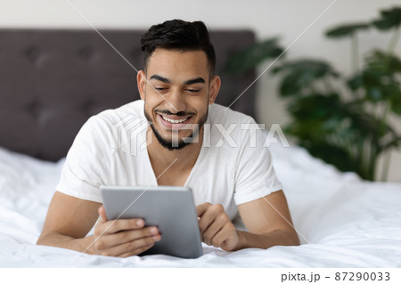 Handsome Arab Guy Browsing Internet On Digital Tablet While Relaxing In Bed Handsome Arab Guy Browsing Internet On Digital Tablet While Relaxing In Bed 87290033