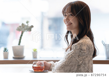カフェの窓辺の席で紅茶を飲んでいる若い女性 87290754