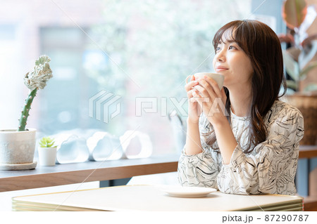 窓辺の席でコーヒーを飲んでいる若い女性 窓辺の席でコーヒーを飲んでいる若い女性 87290787