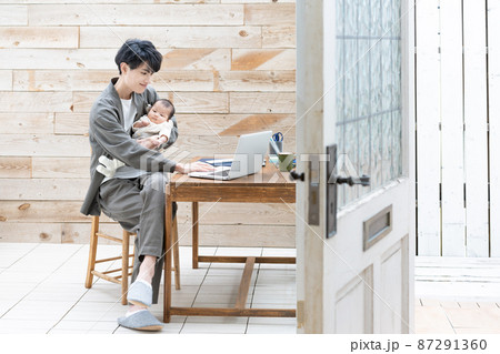 赤ちゃんを抱いてリモートワークをする若い男性 87291360