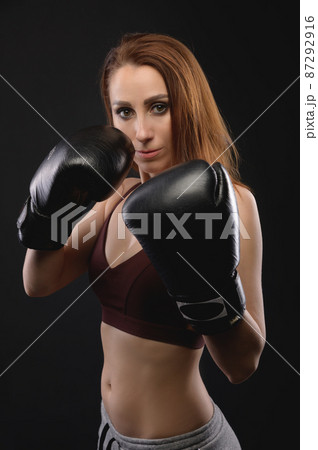 Strong and strict caucasian woman fighter in sportswear and boxing gloves on a black background. Feminism and combat sports Strong and strict caucasian woman fighter in sportswear and boxing gloves on a black background. Feminism and combat sports 87292916