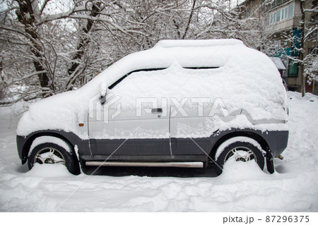A small grey car covered with snow in a winter CIS city 87296375