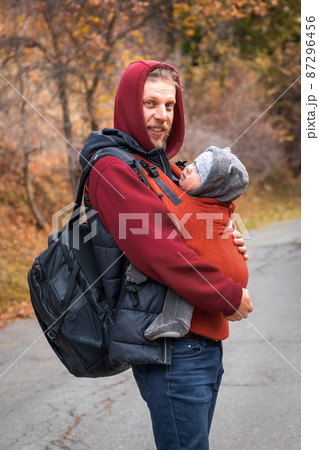 Young bearded babywearing father with his baby in sling autumn walking 87296456