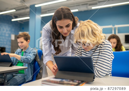 Woman touching tablet screen of boy sitting at desk Woman touching tablet screen of boy sitting at desk 87297089