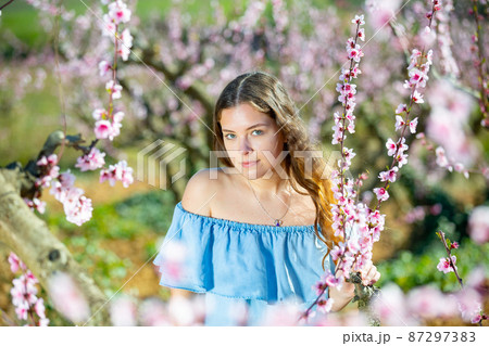 Portrait of an attractive girl in blue dress in blooming peach garden Portrait of an attractive girl in blue dress in blooming peach garden 87297383