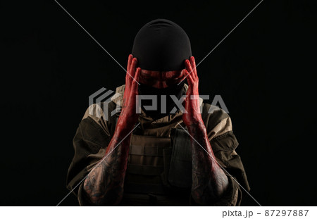 photo of a man in a military uniform and balaclava with a bloody face and hands up to the elbow in blood on a black background photo of a man in a military uniform and balaclava with a bloody face and hands up to the elbow in blood on a black background 87297887