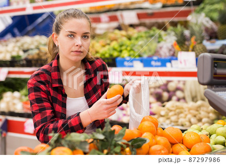 Portrait of young woman buying tangerines at grocery store Portrait of young woman buying tangerines at grocery store 87297986