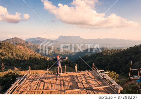 Cheerful asian man standing and enjoying the mountain view from balcony viewpoint in the evening at countryside 87298207