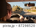 unrecognizable blonde woman driving a car on the road 87298520