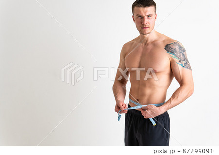 A man measures the waist of a metre and poses against a white background isolated fit muscular background, healthy female bodybuilding woman weight, healthy Oss nutrition athlete, adult sport A man measures the waist of a metre and poses against a white background isolated fit muscular background, healthy female bodybuilding woman weight, healthy Oss nutrition athlete, adult sport 87299091