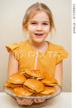 a little girl makes a wish and blows out a candle on a hamburger cake. 87299601