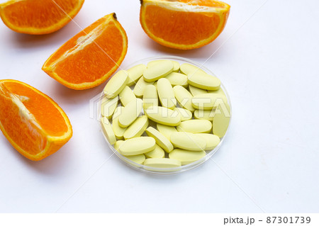 Vitamin c pills with orange fruit on white background. 87301739