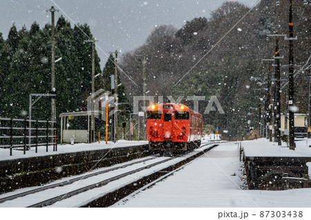 粉雪舞う秘境駅に到着するローカル列車 87303438