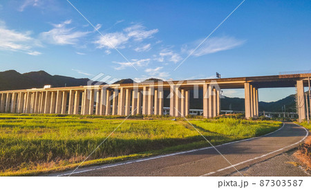 田畑の中にある夕日に照らされる高架高速道路と青空その奥には新幹線 田畑の中にある夕日に照らされる高架高速道路と青空その奥には新幹線 87303587