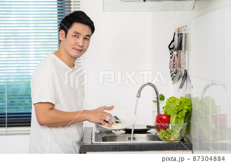 happy man washing dishes in the sink in the kitchen at home happy man washing dishes in the sink in the kitchen at home 87304884