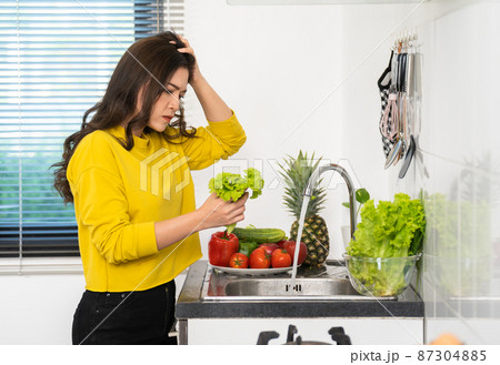 stressed woman washing vegetables in the sink in the kitchen at home stressed woman washing vegetables in the sink in the kitchen at home 87304885