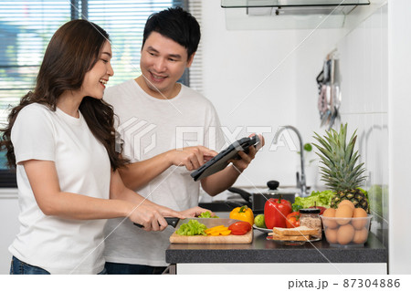 couple cooking and preparing vegetables according to a recipe on a tablet computer in kitchen at home couple cooking and preparing vegetables according to a recipe on a tablet computer in kitchen at home 87304886