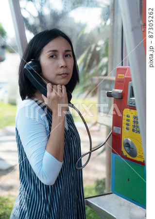 Woman using oldstyle plublic pay phone in telephone booth. 87305262