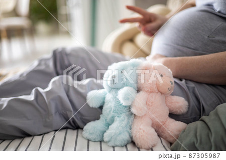 Closeup pregnant female tummy with bear toys gesturing two fingers awaiting twins baby boy and girl Closeup pregnant female tummy with bear toys gesturing two fingers awaiting twins baby boy and girl 87305987