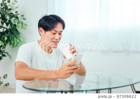 部屋でスマホを見る男性（微笑み） 87306622