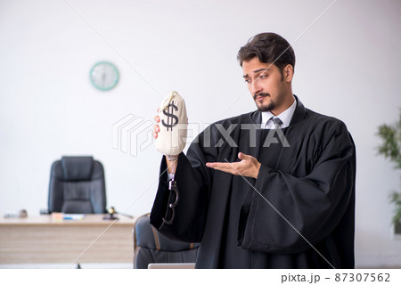 Young male judge holding moneybag in corruption concept 87307562